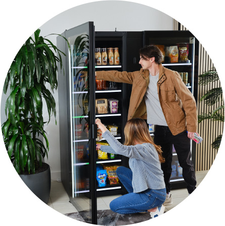 Two people choosing snacks and drinks from a vending machine